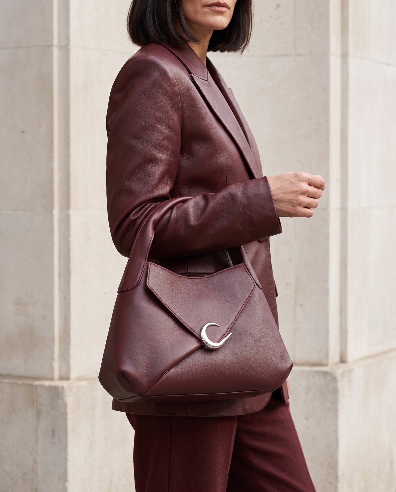 Burgundy handbag styled with matching tailoring against pale stone